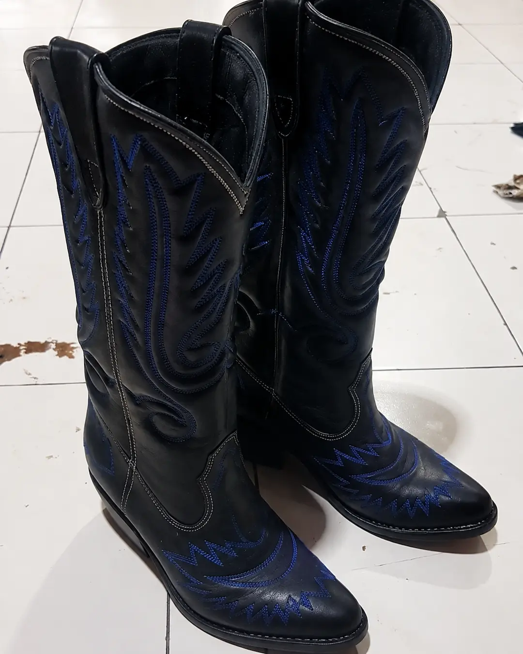 Close-up detail of the blue embroidery on the black cowboy boots.